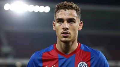 Mid-shot of a 21-year-old Club Brugge forward, athletic build, intense expression, head-and-shoulders framed, wearing the...