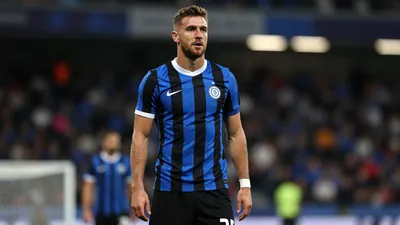 A photorealistic image of a 25-year-old male footballer in a blue and black jersey, with a white collar and black shorts...