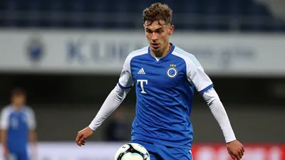A photorealistic image of a 21-year-old German player in a blue jersey with white sleeves, playing for Club Brugge, with...
