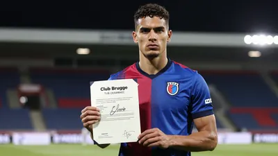 Mid-20s muscular Club Brugge midfielder, waist-up, blue-red home jersey with crisp crest on left chest, holding a signed...