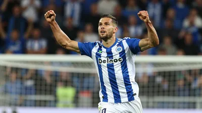 A dynamic action shot of a Cercle Brugge player in a blue and white striped jersey, mid-air, celebrating after scoring a...