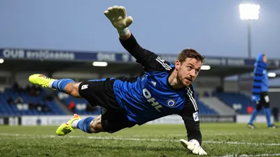 A tight action crop of an anonymous Club Brugge goalkeeper, aged 25-30, in a blue-black jersey, with a white goalkeeper's...