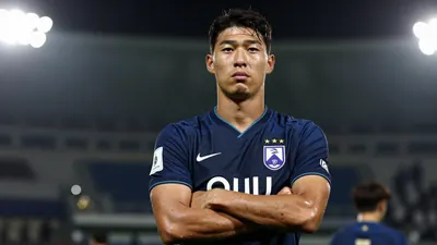 A 24-year-old South Korean defender in a dark blue football kit, standing confidently with arms crossed, looking determined