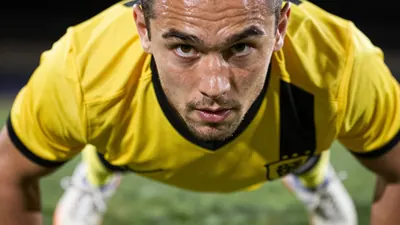 A 26-year-old midfielder with a rugged build, wearing a yellow and black jersey with a smooth, unbroken fabric, and a...